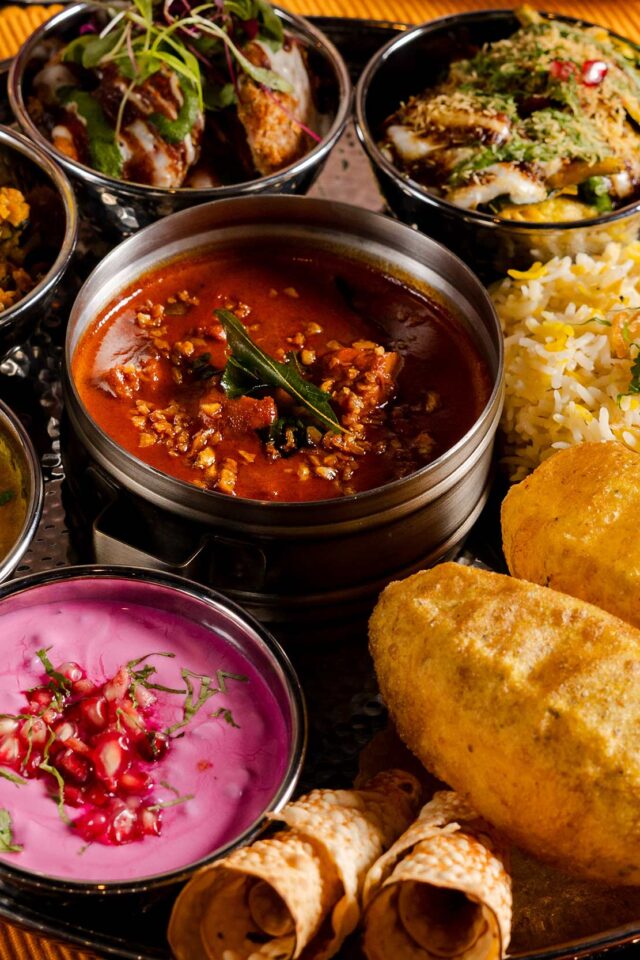 A close-up view of the Diwali feasting thali at Bombay Bustle showcasing a central curry dish surrounded by colourful sides, rice, and freshly fried puri bread