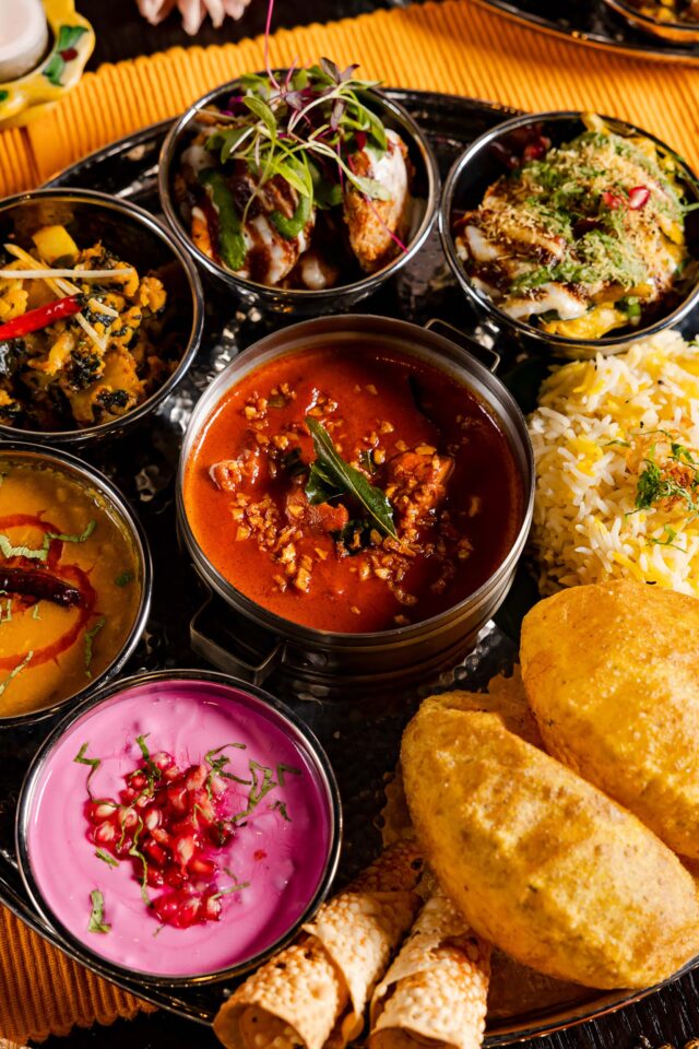 A festive Diwali feasting thali at Bombay Bustle featuring an assortment of curries, dal, pink pomegranate raita, rice, and puffed puri bread on a silver platter