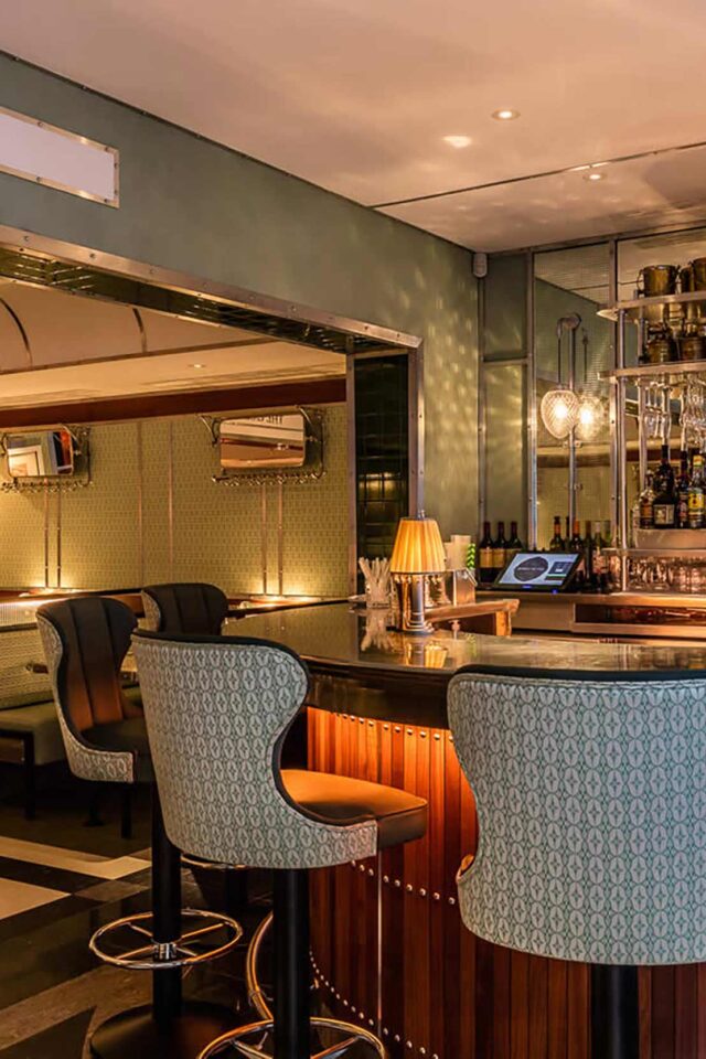 The elegant bar, featuring rich jacquard and leather stools set against vintage railway-inspired.
