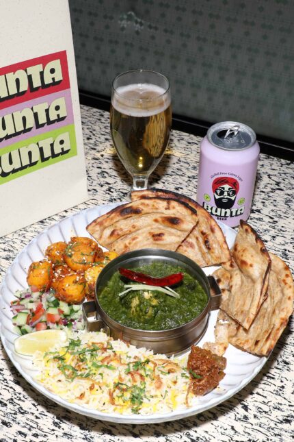 A delicious Indian Bustle Bowl with green curry, rice, naan, and spiced potatoes, served with a can and glass of Bunta Beer at Bombay Bustle in Oxford Circus.